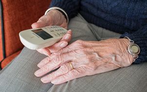 dłonie starszej osoby trzymającej w prawym ręku telefoniczny aparat bezprzewodowy najprawdopodobniej wybierającej numer