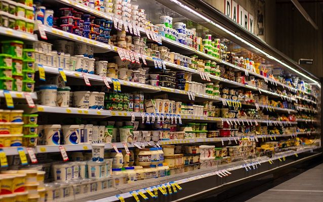 wpół otwarta lodówka sklepowa w supermarkecie z wieloma asortymentami produktów spożywczych, z dużą ilością wywieszek cenowych, podświetlona