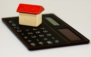 drewniany klocek w kształcie  domku z czerwonym dachem stojący na czarnym kalkulatorze elektronicznym