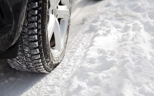 zdjęcie przedstawia koło samochodowe z cześcią nadwozia samochodu. Czarna, obleczona śniegiem oponę samochodową znajdującą się na srebrnej alufeldze.  Auto znajduje się na śniegu.