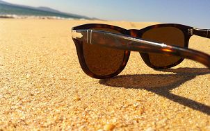 Brązowe okulary przeciwsłoneczne w rogowej oprawce leżące na złotym piasku. Image by cesardv from Pixabay