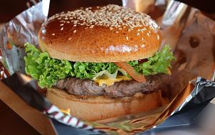 Hamburger w bułce posypanej sezamem, z warzywami, żółtym serem znajdujący się w folii aluminiowej  Zdjęcie wykonane przez Daniel Mačura (źródło: Pixabay)